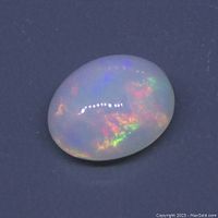 Close-up image of the opal gemstone showing the white base and multicolour play of colour on a dark background.