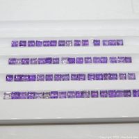 Top-down view of four rows of square purple amethyst stones on display white background.