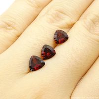 Three trilion-shaped garnet stones placed on a hand showing size scale and color.