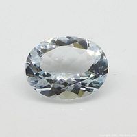 Clear oval faceted aquamarine gemstone laying on white background, showing transparency and facets.