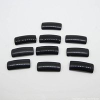 Top-down view of ten polished black onyx saddle cut stones arranged neatly to show shape and finish.