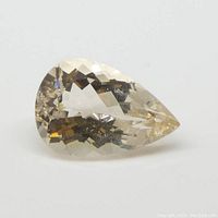 Pear-shaped Morganite gemstone resting on a white surface showing orangy pink facets and transparency.