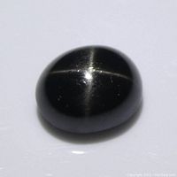 Close-up photo of the oval cabochon black star diopside gemstone showing the star-shaped light reflection pattern.