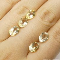 Five oval yellow citrine gemstones displayed on fingers showing size and color.