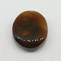 Top view of oval cabochon fire agate gemstone showing smooth polished surface and brown-orange coloration