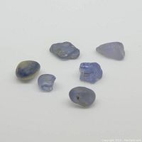 Six rough unheated blue sapphire gemstones arranged on white background, showing size and shape variation