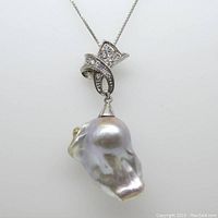 Front view of baroque pearl pendant hanging from sterling silver decorative setting and chain against white background.