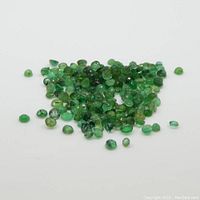 Loose round green emerald gemstones piled on white surface
