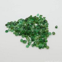 Pile of small round green emerald gemstones on white background