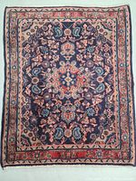Full view of rectangular hand knotted Persian rug showing floral medallion and complementary border in blue, red, beige.