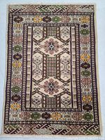 Full view of the hand knotted wool rug showing detailed geometric and floral design in beige, brown, green, yellow, and pink colors.