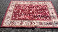 Full view of the red floral pattern area rug placed on an asphalt surface, showing size and design.