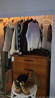 Multiple coats hanging on closet rod; boots and bag displayed on a stool below