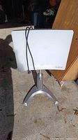 Front view of the rectangular white light panel on its silver three-legged stand with power cord.