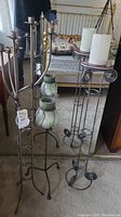 Three metal floor candle holders of varying height by a mirror and a bed frame.