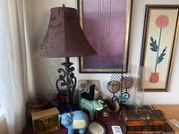 Photo showing a decorative table lamp with a brown patterned shade, various small decor items including piggy banks, a wooden carved horse, and a green ceramic elephant figurine on a table against wall art.
