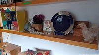 Shelf with painted wooden box, CDs, decorative plate, desk lamp and assorted decor items including vases, baskets, flowers and plush bird.
