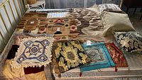 Full view of multiple pillows and macrame textile pieces arranged on a mattress including the largest macrame tapestry and throw pillows with diverse bohemian patterns.