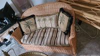 Front view of the wicker love seat showing woven wicker frame, striped cushions and three decorative palm tree pillows.