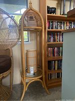 Full view of tall wicker plant stand with glass shelf and attached lamp in a cozy room environment.