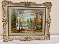 Front view of the framed oil painting depicting a lakeside landscape with a stone path and trees, showing the overall scene and frame detail.