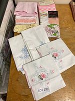 Photo showing a variety of pillowcases including embroidered white ones, pink lace-trimmed, and packaged muslin pillowcases.