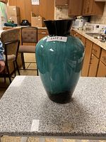 Two photos of a large Blue Mountain Pottery vase placed on a kitchen counter. The vase has a bulbous body with a black flared rim and a teal to black gradient glaze.