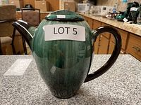 Front angle view of teapot with lid on, showing the dark green to black gradient glaze with dark brown handle and spout.