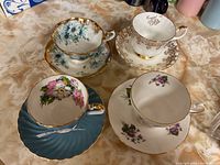 Four bone china cups and matching saucers displayed together on a countertop, showing their floral patterns and gold trim