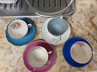 Top view of three bone china teacups with their matching saucers placed on a countertop, showing colors and floral designs.