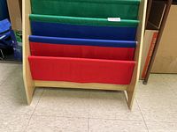 Front view of the child's book stand showing three fabric pockets in green, blue, and red.