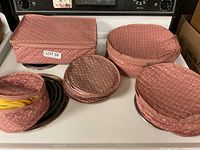 Full set of five pink quilted china storage protectors in varying shapes and sizes arranged on a stove.