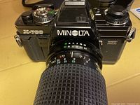 Front view of Minolta X-700 camera with attached lens showing controls and model name on top plate and body