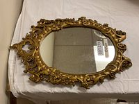 Full view of the gold ornate oval mirror on a white cloth, showing its shape and decoration.