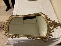 Full top view of the ornate gold framed mirror on a white cloth covering a table.