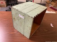 Front view of vintage wooden butter box showing pale green paint and wear marks on table.