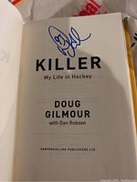 Title page of the book showing Doug Gilmour's autograph in blue ink above the title 'Killer My Life in Hockey' by Doug Gilmour with Dan Robson.