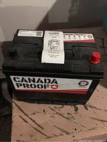 Front and top view of the Canada Proof car battery with branding and cranking amps information visible.