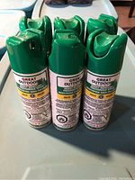 Six green cans of Great Outdoors Insect Repellent spray arranged on a table, showing front and back labels with warning and usage instructions.