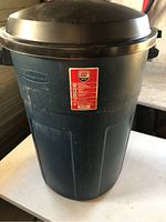 Front view of the Rubbermaid Roughneck 98L garbage can showing the brand logo and red label on the front surface, lid attached.