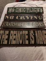 Four wooden man cave signs laid out on a white sheet, each with humorous statements for man cave decoration.