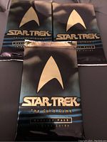 Photo of three sealed Star Trek The Card Game booster packs arranged for display showing front packaging.