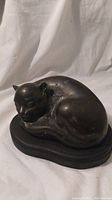 Bronze cat statue angled showing curled sleeping position and some surface tarnish.