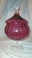 Cranberry glass candy compote with ribbed design and pointed lid on a clear pedestal base.