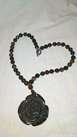 Full view of the necklace laid flat showing the carved rose pendant and multi-colored round jade beads.