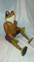 Front three-quarter view of the large wooden frog puppet showing jointed limbs, painted face and clothing detail.