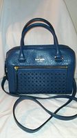 Front view of blue leather Kate Spade handbag showing perforated front pocket with gold zipper and logo.
