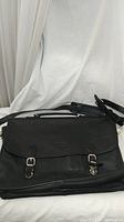 Full view of the black pebble leather briefcase showing front flap and adjustable shoulder strap.
