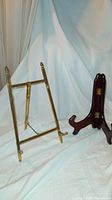 Brass and wooden small foldable easels side by side on white fabric background