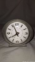 Front view of vintage alarm clock showing dial with numbers and hands, condition, and brand markings.